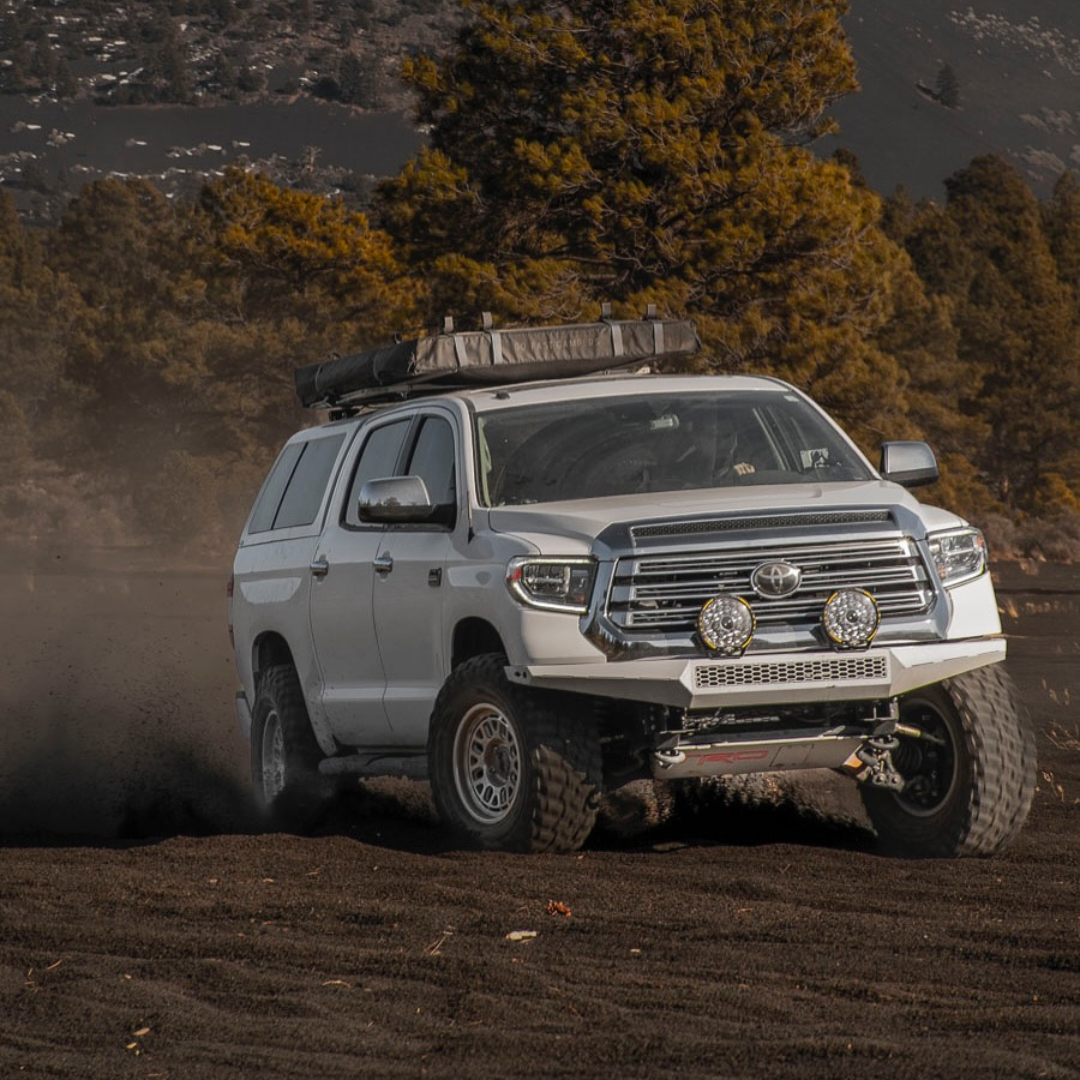 Silver SUV driving on a dirt road with trees and mountains in the background