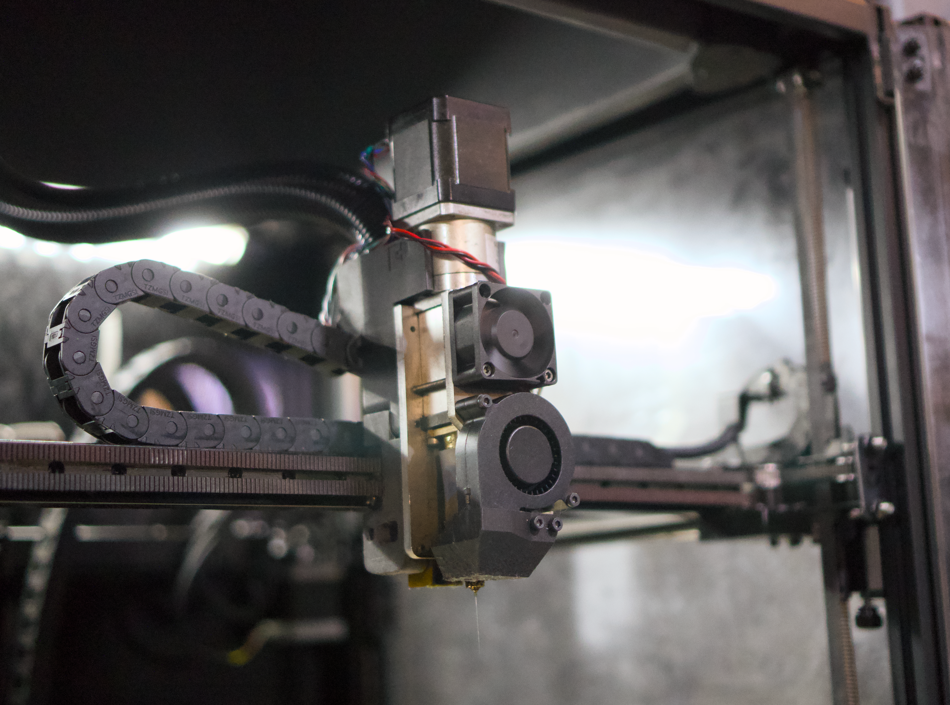 Close-up of a 3D Printer with a chain mechanism inside a dark enclosure.